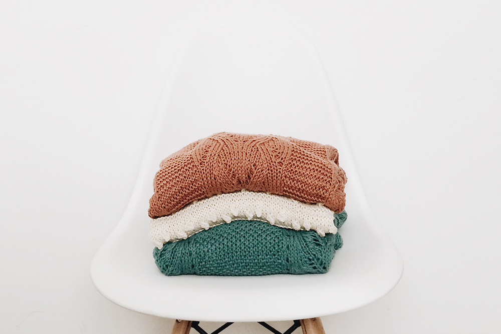 folded sweaters on white chair with white background