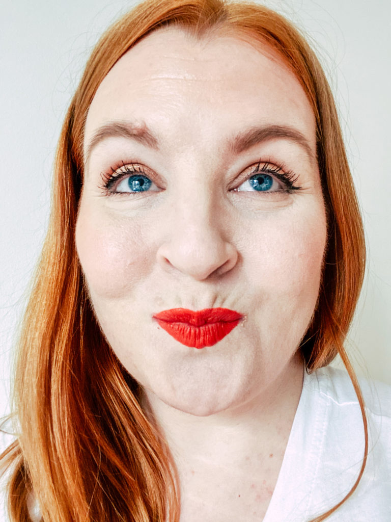 A headshot of Mifa, with her red hair down wearing bright red gluten-free lipstick